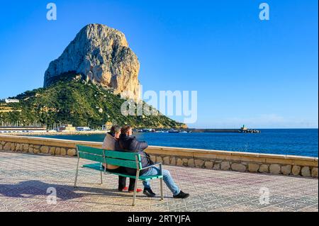 Calpe, Spanien - 10. Januar 2023: Ein Paar sitzt auf einer Bank und blickt auf den Strand Stockfoto