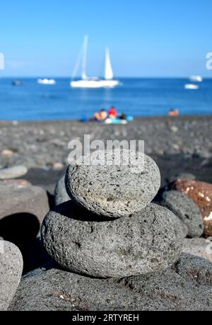 Lavasteine, Kieselsteine am Strand, Meer mit Boot im Hintergrund, Stromboli Insel, Italien, Europa Stockfoto