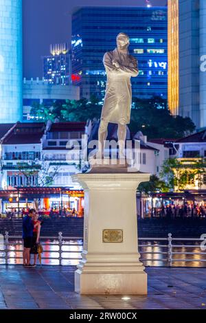 Ein nächtlicher Blick auf die Statue von Sir Stamford Raffles am Nordufer des Singapore River, die an Raffles Ankunft in Singapur im Jahr 1819 erinnert. Stockfoto