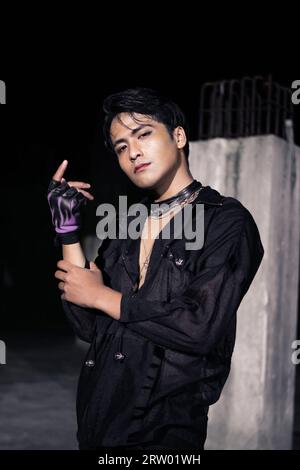 Ein asiatischer Mann kleidete sich in schwarz-schwarzes Haar und posierte als männlich vor einer Gebäudesäule Stockfoto