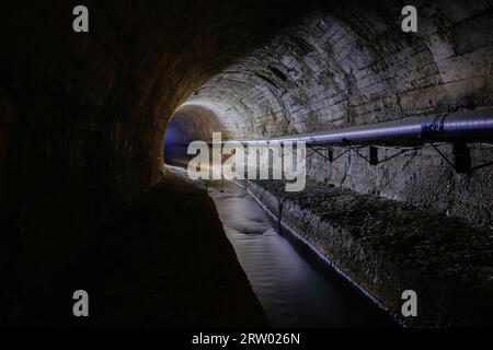 Unterirdischer, gewölbter städtischer Abwassertunnel mit schmutzigem Abwasser. Stockfoto