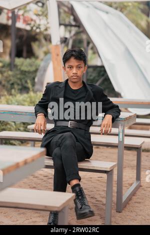 Ein asiatischer Teenager in einer schwarzen Jeansjacke posiert auf einem Café-Stuhl und entspannt sich am Nachmittag Stockfoto