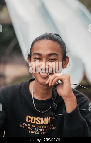 Ein asiatischer Mann, der seine Haare zusammengebunden hat und eine schwarze Pulli-Jacke trägt, sitzt entspannt am Kaffeetisch, wenn er seine Freunde am Nachmittag trifft Stockfoto