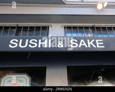 Allgemeines Sushi und Sake in weißen Großbuchstaben auf verwitterter und getragener schwarzer Leinwand über einem japanischen Restauranteingang; asiatische Speisen und Getränke. Stockfoto
