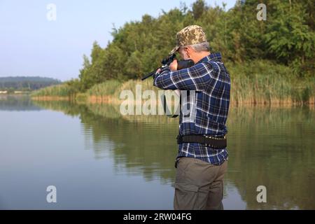 Mann mit Jagdgewehr in der Nähe des Sees im Freien. Leerzeichen für Text Stockfoto