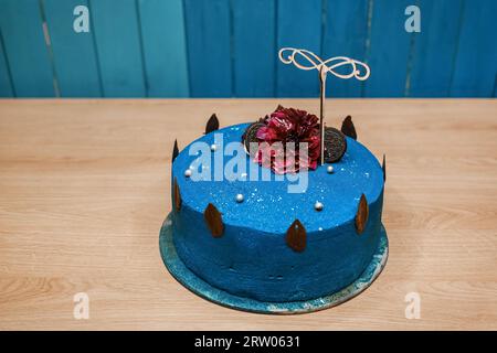 Festlicher süßer köstlicher Kuchen mit dekorativem Geburtstagsgeschenk in Blaucremefarben steht auf einem Holztisch. Stockfoto