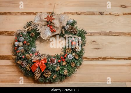 Weihnachtskranz aus künstlicher Fichte, Kiefernnadeln, verziert mit Kegeln und Spielzeug auf einem hölzernen Hintergrund. Stockfoto