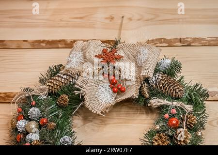 Weihnachtskranz aus künstlicher Fichte, Kiefernnadeln, dekoriert mit Kegeln und Spielzeug auf einem hölzernen Hintergrund, Nahaufnahme. Stockfoto