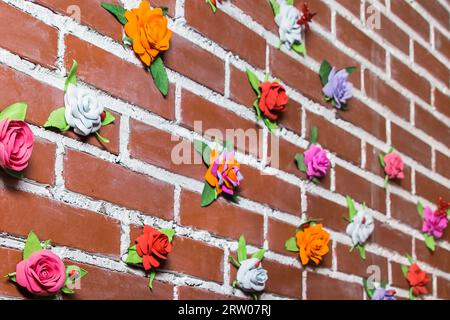 Die Backsteinmauer ist mit künstlichen Objekten, Blumen, mehrfarbigen Rosen, dem Inneren dekoriert. Stockfoto