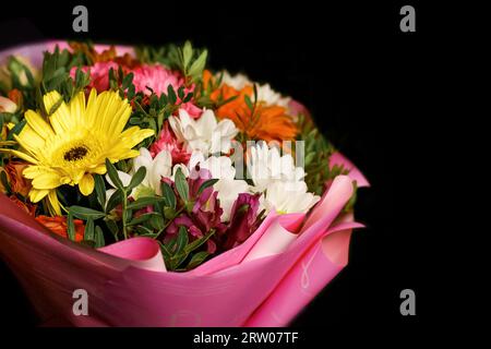 Blumenstrauß mit bunten, hellen Chrysanthemen-Blüten in einer Geschenkbox aus rosa Farben auf dunklem Hintergrund. Stockfoto