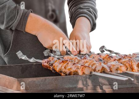 Die Hände des Mannes kochen Kebab auf Spießen über dem Grill, beobachten das Fleisch, bis es vollständig gekocht ist. Stockfoto