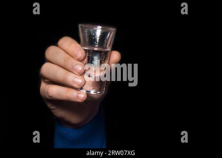 Die Hand eines Mannes hält ein Glas alkoholgekühlten Wodka auf schwarzem Hintergrund. Stockfoto