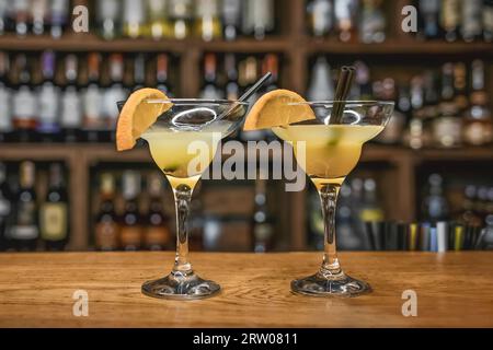 Zwei alkoholische Cocktails mit Orangensaft und ein dekoriertes Glas mit Strohhalm auf einer hölzernen Bartheke vor dem Hintergrund eines Nachtclubs. Stockfoto