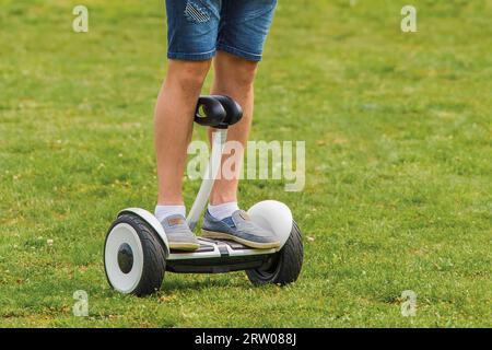 Die Beine eines erwachsenen Mannes stehen auf einem Hoverboard vor dem Hintergrund von Gras im Park. Stockfoto