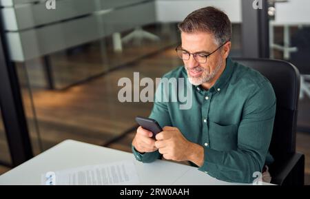 Lächelnder, geschäftiger Geschäftsmann, der im Büro auf dem Smartphone arbeitet. Stockfoto