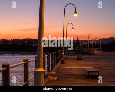 Orange Sky, Coffs Harbour Jetty bei Sonnenuntergang, geschwungene Bäume leuchten auf Stockfoto