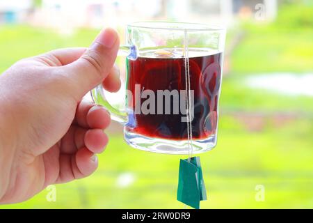 Eine Tasse heißen Tee in der Hand eines Mannes im Freien. Mann, der heißen Tee mit einem Teebeutel hält Stockfoto