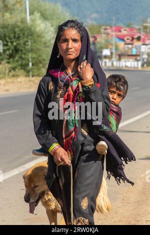 Anantnag, Indien. September 2023. Eine Kaschmir-Nomadenfrau, die vor dem Winter ein Kind auf dem Rücken in wärmere Ebenen trägt, in der Gegend von Kokernag, etwa 100 km von Srinagar entfernt. Jedes Jahr reisen Tausende nomadischer Bakerwal- und Gujjar-Familien in die Hochwiesen Kaschmirs und bleiben dort für die Sommermonate, um Vieh zu weiden. Sie fahren vor dem Winter im Oktober zurück in die wärmeren Ebenen. (Foto: Faisal Bashir/SOPA Images/SIPA USA) Credit: SIPA USA/Alamy Live News Stockfoto