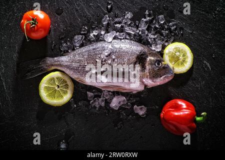 Dorade mit Zitronen und Tomaten auf schwarzem Schiefer Stockfoto