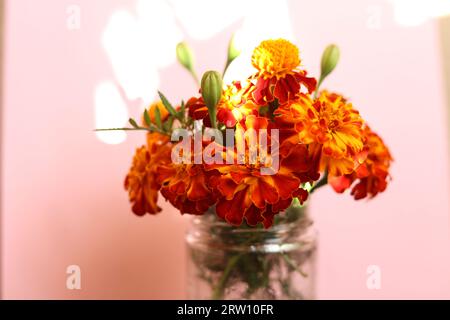 Ein Blumenstrauß aus leuchtend orangen und gelben Tagetes patula, die französischen Ringelblumen in einem Glas Stockfoto
