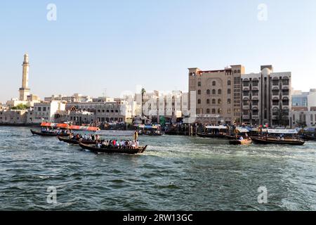 Blick über den Dubai Creek von Deira nach Bur Dubai. Abras, die typischen Wassertaxis in Dubai, fahren auf dem Fluss. Das Minarett der Großen Moschee Stockfoto