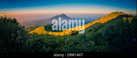 Panorama-Foto von Bergen und Mount Merbabu bedeckt mit Sonne und Nebel bei Sonnenaufgang in der Nähe von Yogya in Zentral-Java Provinz in Indonesien. In diesem Stockfoto