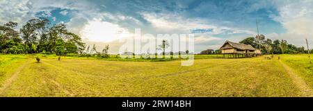 Panoramafotografie des Grasfeldes mit einfachen Häusern aus Stroh und Holz in Palembe, Fluss Sepik in Papua-Neuguinea Stockfoto