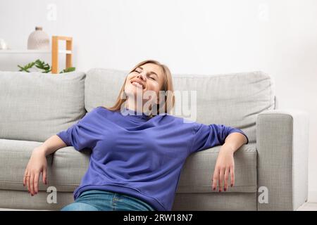 Eine glückliche Frau entspannt sich auf dem Sofa, atmet kühle Luft aus der Klimaanlage, genießt das komfortable Klima im belüfteten Wohnzimmer, ich Stockfoto