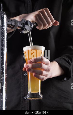 Der Barkeeper gießt frisches Bier aus dem Fass in ein Glas auf dunklem Hintergrund. Hochwertige Fotos Stockfoto