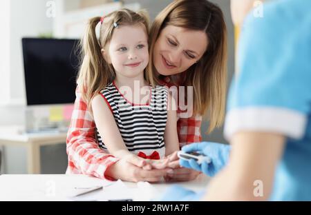 Der Arzt überprüft den Blutzuckerspiegel des kleinen Mädchens mit einem digitalen Glucometer im Krankenhaus Stockfoto