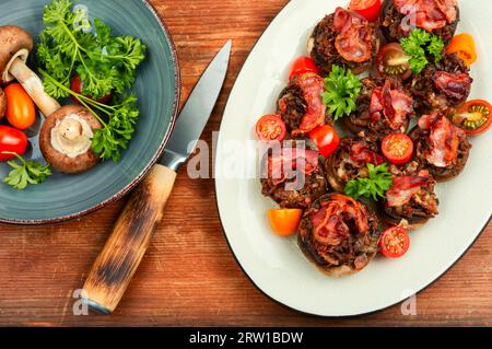 Leckere Champignon-Pilze, gefüllt mit Fleisch, Tomaten und Speck auf rustikalem Holzgrund. Draufsicht. Stockfoto