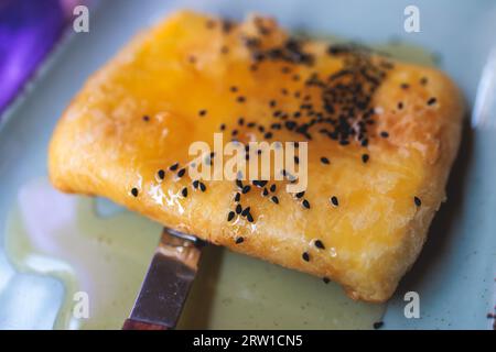 Gebratener Fetakäse in Phyllo-Gebäck mit Honig und Sesam, traditioneller griechischer Vorspeise auf einem Teller, serviert in einer traditionellen Taverna-Café-Pause Stockfoto