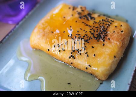 Gebratener Fetakäse in Phyllo-Gebäck mit Honig und Sesam, traditioneller griechischer Vorspeise auf einem Teller, serviert in einer traditionellen Taverna-Café-Pause Stockfoto