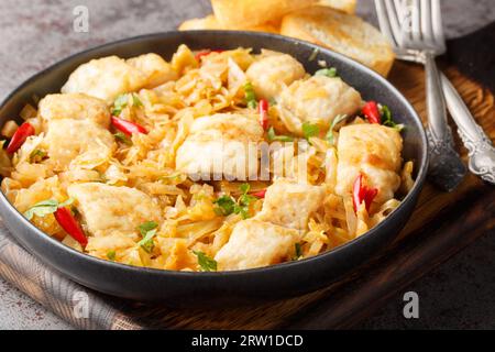 Köstlicher würziger gedünsteter Weißkohl mit Meeresfischfilet, Zwiebeln und Chilipfeffer aus nächster Nähe auf einem Teller auf dem Tisch. Horizontal Stockfoto