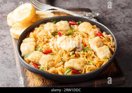 Gedünsteter Weißkohl mit Meeresfischfilet, Zwiebeln und Chilipfeffer aus nächster Nähe auf einem Teller, der mit Toast auf dem Tisch serviert wird. Horizontal Stockfoto