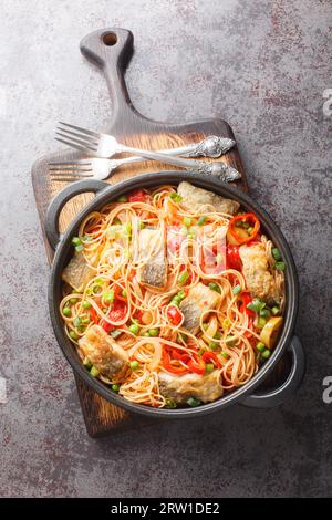 Mediterrane Spaghetti mit weißem Meeresfisch, Gemüse und Tomatensauce aus nächster Nähe in einer Pfanne auf dem Tisch. Vertikale Draufsicht von oben Stockfoto