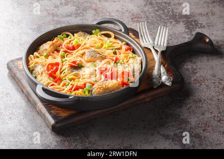 Spaghetti-Auflauf mit weißem Meeresfisch, Paprika, Zwiebeln, grünen Erbsen und Tomatensauce aus nächster Nähe in einer Pfanne auf dem Tisch. Horizontal Stockfoto
