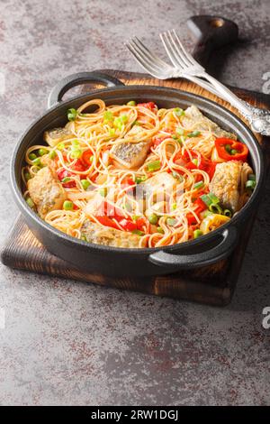 Spaghetti mit weißem Meeresfisch, Paprika, Zwiebeln, grünen Erbsen, Knoblauch und Tomaten aus der Nähe in einer Pfanne auf dem Tisch. Vertikal Stockfoto