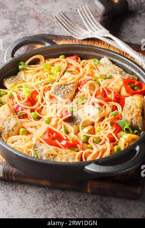 Spaghetti-Nudeln mit weißem Meeresfisch, Paprika, grünen Erbsen, Knoblauch und Tomaten aus nächster Nähe in einer Pfanne auf dem Tisch. Vertikal Stockfoto