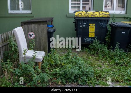 09.07.2023, Deutschland, Bremen, Bremen - Mülltonne vor einem Wohnhaus, davor ein wild entsorgter Stuhl. 00A230709D099CAROEX.JPG Stockfoto