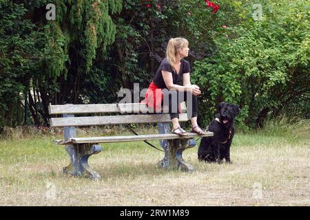 25.06.2022, Deutschland, Brandenburg, Dranse - Frau sitzt neben ihrem Hund auf der Rückseite einer Parkbank. 00S220625D063CAROEX.JPG [MODELLVERSION: JA, PRO Stockfoto
