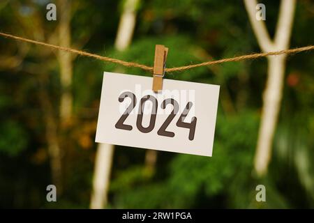 2024 auf Papier, das an Juteseil hängt. Auf Wiedersehen 2023 Hello Happy New Year 2024 Concept. Stockfoto