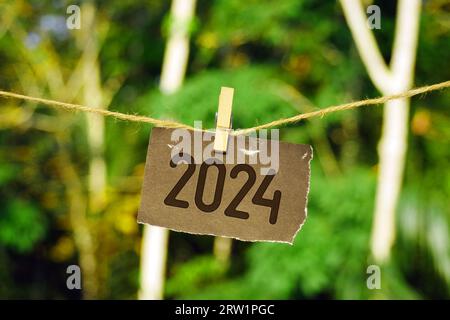 2024 auf Papier, das an Juteseil hängt. Auf Wiedersehen 2023 Hello Happy New Year 2024 Concept. Stockfoto