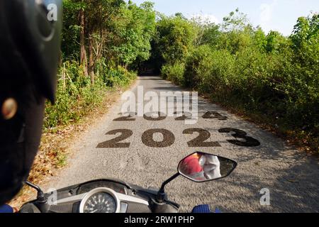 Schwarze Asphaltstraße mit den Neujahrsnummern 2023, 2024 mit Motorradfahrern, die auf einer ruhigen und engen Forststraße vorbeifahren Stockfoto