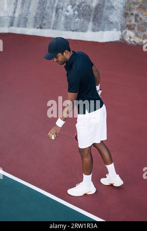 Junger Mann, der den Ball in der Baseline auf dem Hartplatz für den Serve hüpft Stockfoto