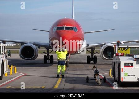 31.03.2023, Deutschland, Brandenburg, Schönefeld - Bodenkontrolleur, der ein Flugzeug der Norwegian Airlines auf seine Parkposition auf dem Vorplatz der BER lenkt Stockfoto