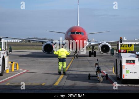 31.03.2023, Deutschland, Brandenburg, Schönefeld - Bodenkontrolleure leiten ein Flugzeug der Norwegian Airlines an seine Parkposition auf dem Vorplatz von BER Ai Stockfoto