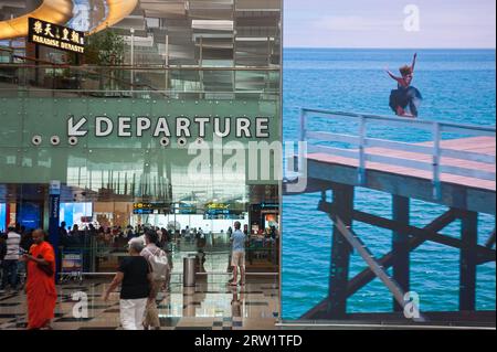 14.02.2018, Singapur, Republik Singapur, Asien - Flugreisende neben einer riesigen digitalen Werbetafel in der Abflughalle am Flughafen Changi T3. Stockfoto