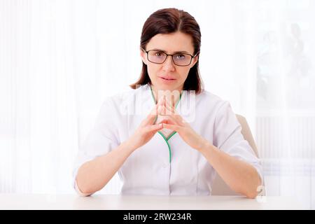 Selige Kinderärztin, die an ihrem weißen Tisch sitzt Stockfoto