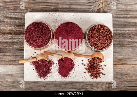 Getrockneter Gewürzsumak in einem Holzlöffel. Gemahlenes Sumakgewürz. Getrocknete gemahlene rote Sumakpulver-Gewürze in Holzlöffel mit Sumakbeeren auf rustikalem Tisch. Gesundheit Stockfoto